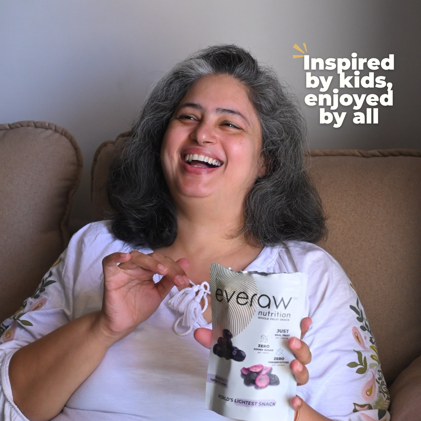 Woman holding a 'everaw kala jamun' snack package, sitting on a couch with text 'Inspired by kids, enjoyed by all'.