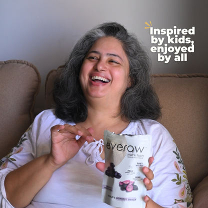 Woman holding a 'everaw kala jamun' snack package, sitting on a couch with text 'Inspired by kids, enjoyed by all'.