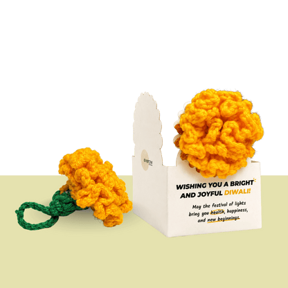 Handmade orange crochet marigold flower with a green stem beside a Diwali greeting card, made by the women of Surabhi, an Ajmer NGO that creates jobs for women with no family support