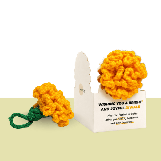 Handmade orange crochet marigold flower with a green stem beside a Diwali greeting card, made by the women of Surabhi, an Ajmer NGO that creates jobs for women with no family support