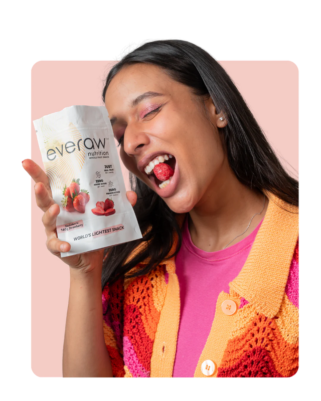 Woman eating a freeze dried strawberry from an Everaw whole fruit snack pack, real fruit crunch with nothing added
